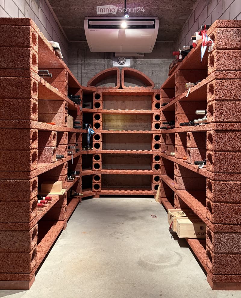 Wine cellar with brick-style wine racks holding multiple bottles, wooden crates on the floor, and an air conditioning unit on the ceiling.
