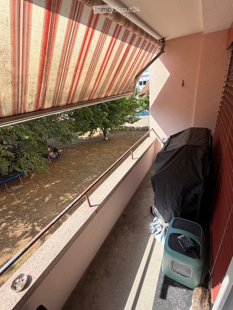 Balcony with striped awning, metal railing, and outdoor items including a covered grill and a small table.