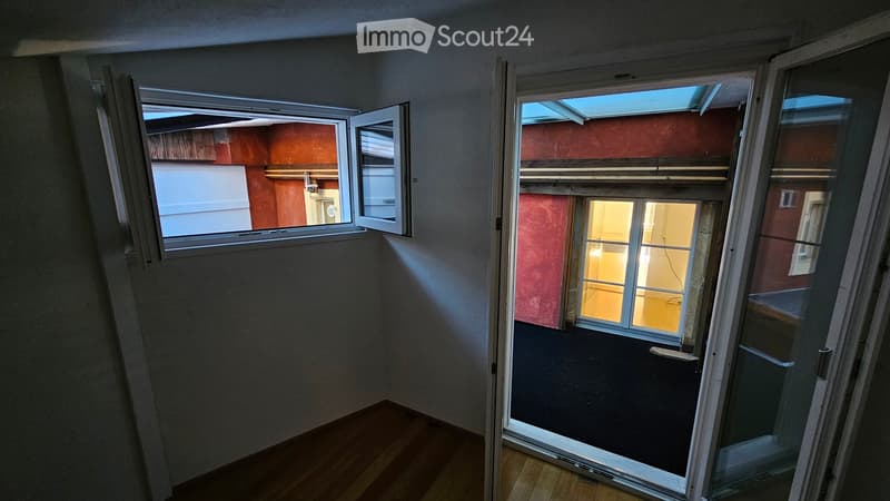 Empty room with wooden flooring, large windows, and a sliding glass door leading to a balcony area.