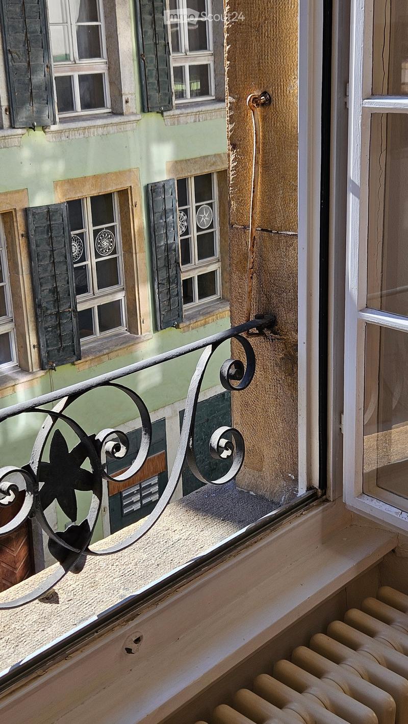 Balcony with ornate metal railing, overlooking a building with multiple windows and shutters.