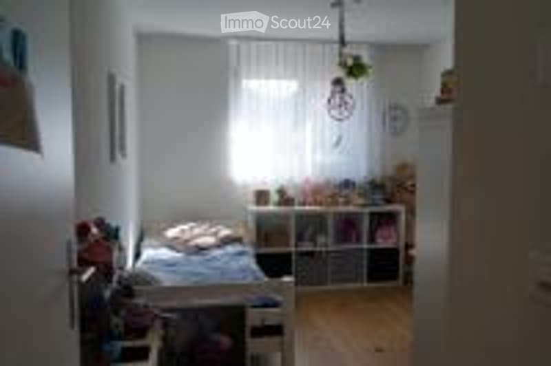 Cozy bedroom with a bed, nightstand, bookshelf, and a hanging lamp. The room features white walls, wooden flooring, and a window with blinds.