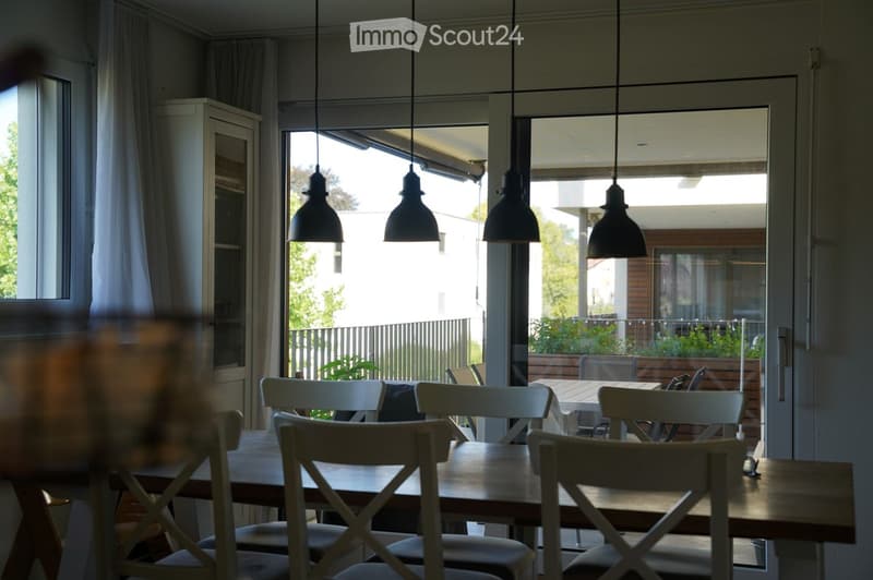 Dining room with wooden table, chairs, and a cabinet, large windows and sliding doors leading to a balcony.