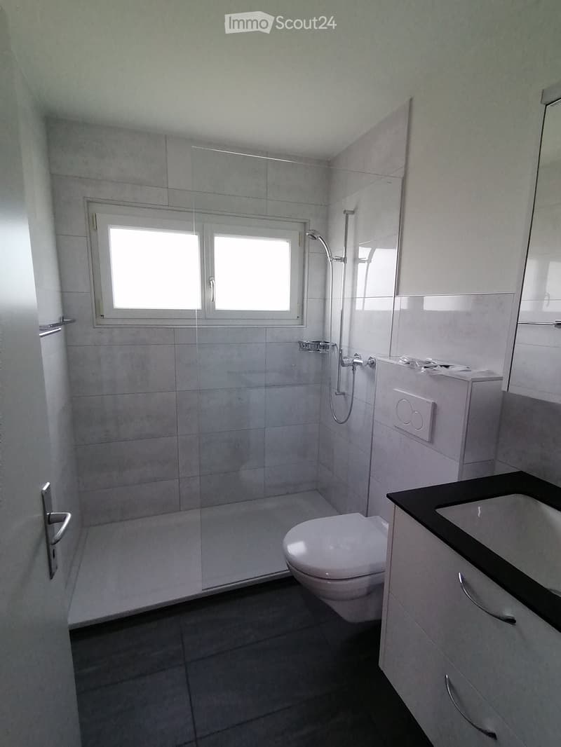 Modern bathroom with white tiles, a glass-enclosed shower, a toilet, a sink with a black countertop, and a white cabinet.