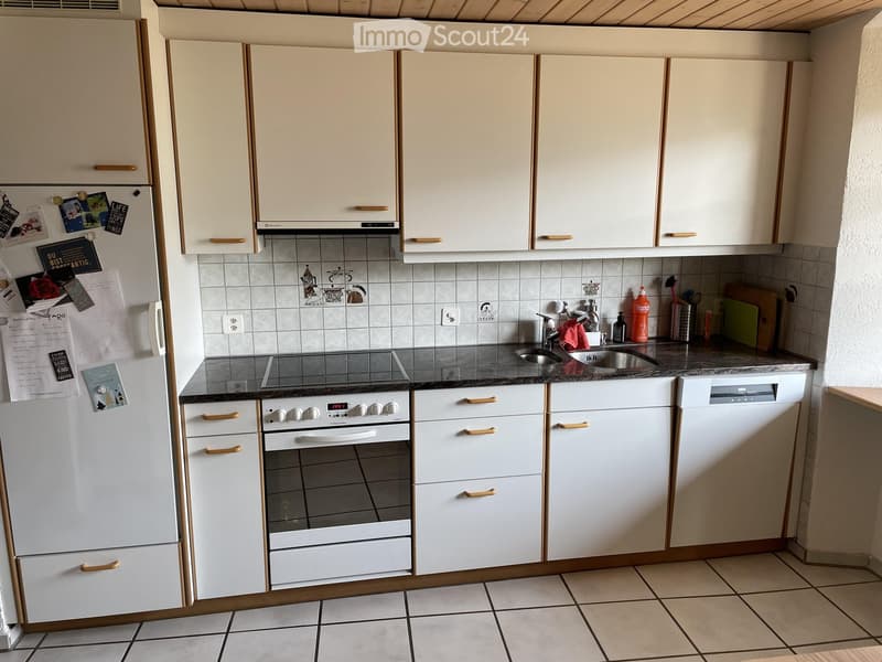 A modern kitchen with white cabinets, a stainless steel sink, an oven, and a dishwasher. The countertops are dark, and the floor is tiled.
