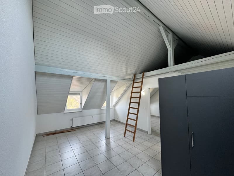 Empty attic space with white wooden slatted ceiling, tiled floor, and large windows. A wooden ladder is positioned against the wall.