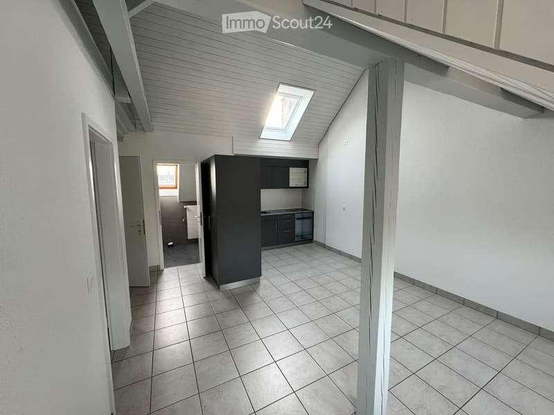 Empty hallway with tiled floor, white walls, and a small kitchen area visible at the end. The ceiling has exposed wooden beams and a skylight.