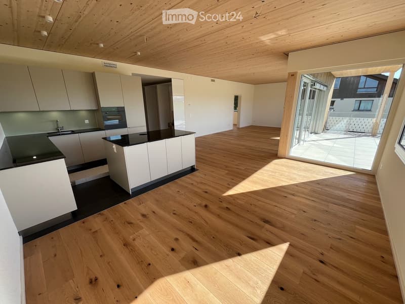 Empty room, hardwood floors, white cabinets, modern kitchen with black countertops, sliding glass door to balcony