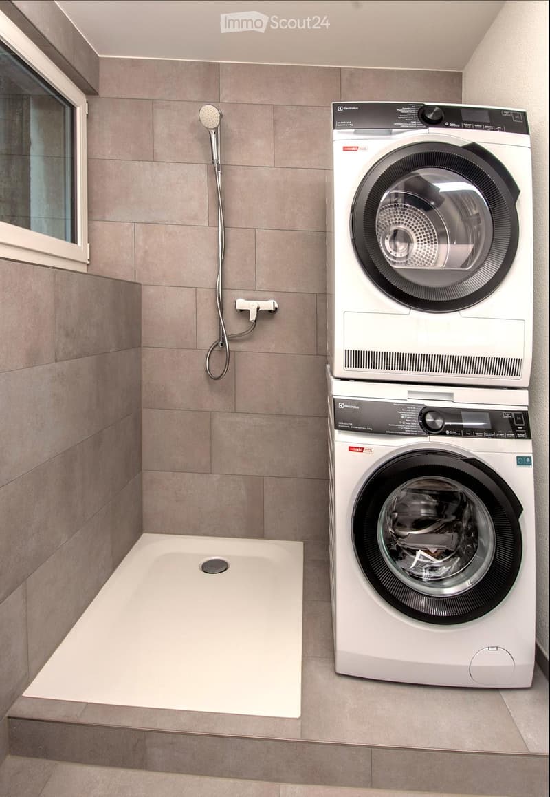 Modern bathroom with a large shower area, a washing machine, and a dryer stacked vertically.