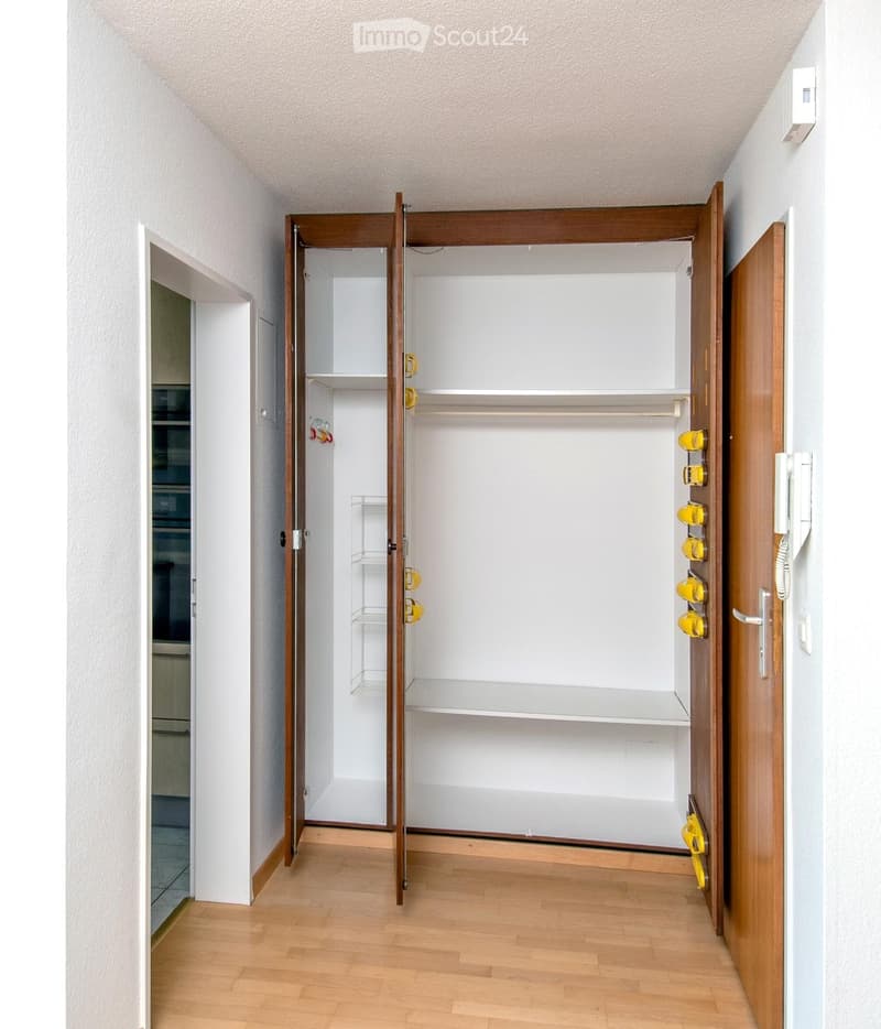 Empty room with wooden floor, white walls, and open closet with wooden frame and shelves.