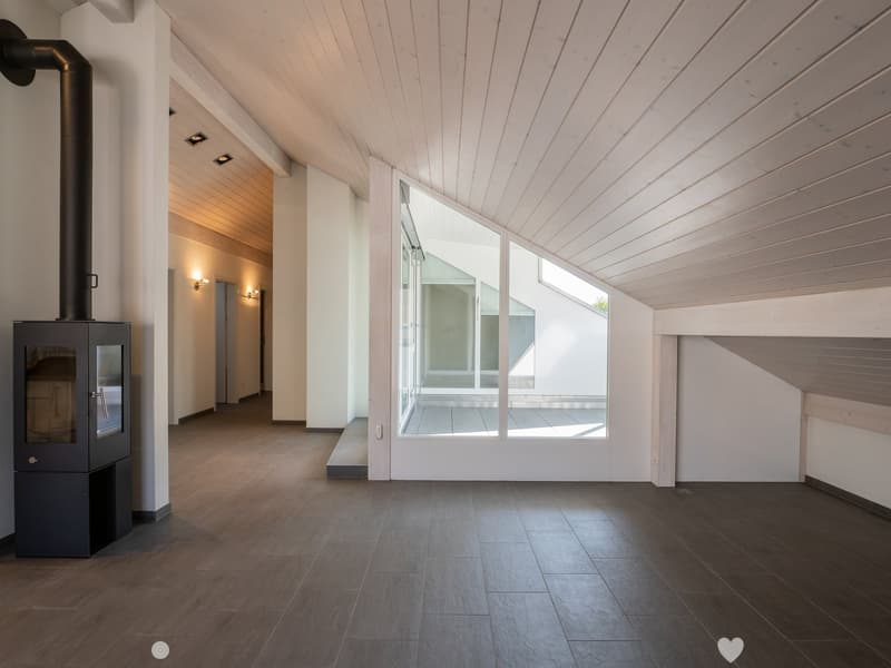 Bright, open space with wooden floors, white walls, and large windows, featuring a modern wood-burning stove and recessed lighting.