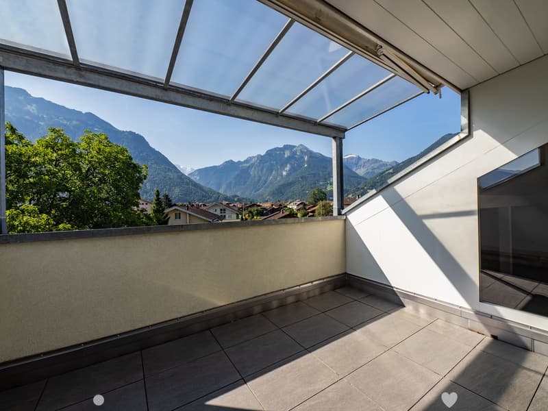 Balcony with tiled floor, glass roof, and scenic mountain view.