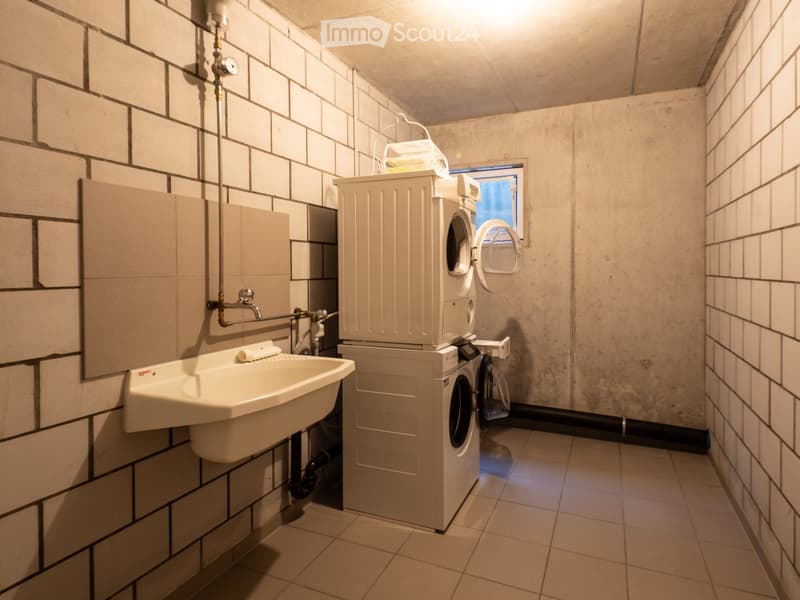 Bathroom with a sink, washing machine, and tiled walls.