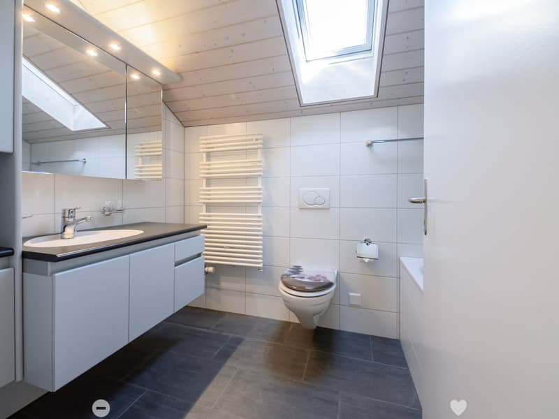 Modern bathroom with white tiles, dark grey floor, sink with faucet, mirror, radiator, toilet, and toilet paper holder.