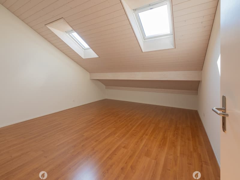 Empty attic room with wooden flooring, white walls, and skylight windows.