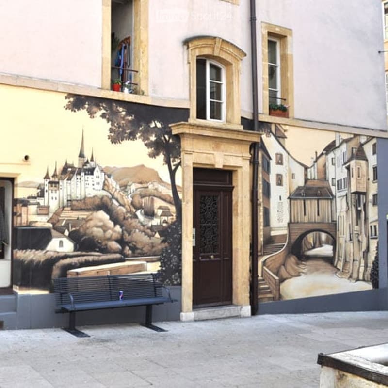 Facade of a building with a large mural depicting a castle and landscape, a bench in front, and windows with flower boxes.