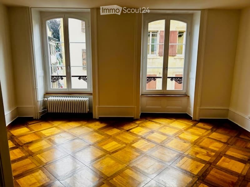 Empty room with wooden floor, large windows, radiator, and white walls.