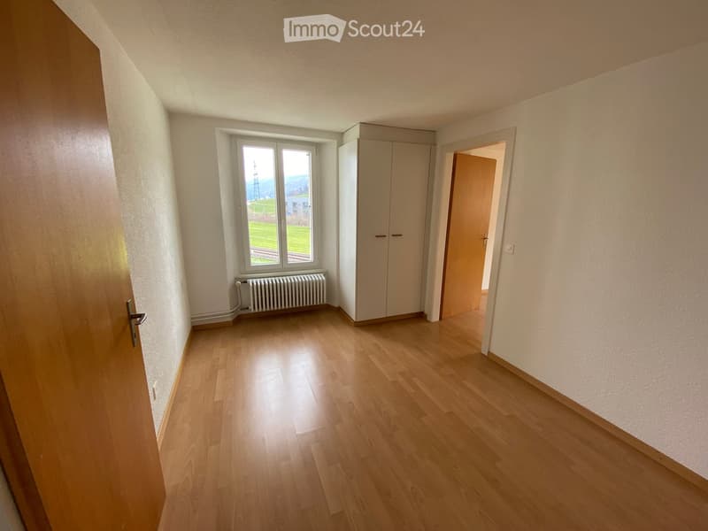 Empty room with wooden flooring, white walls, a window with a view, a radiator, and a built-in closet.