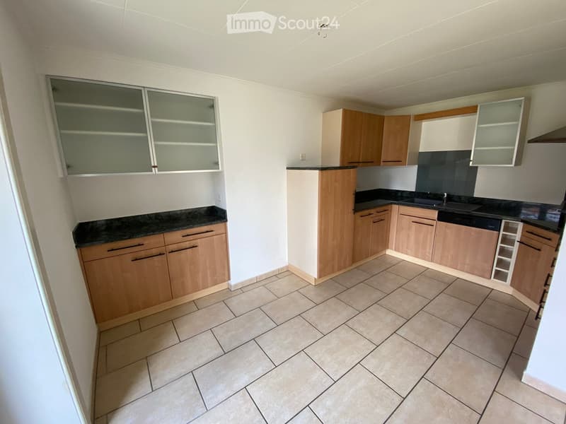 Modern kitchen with light wooden cabinets, black granite countertops, and tiled flooring.