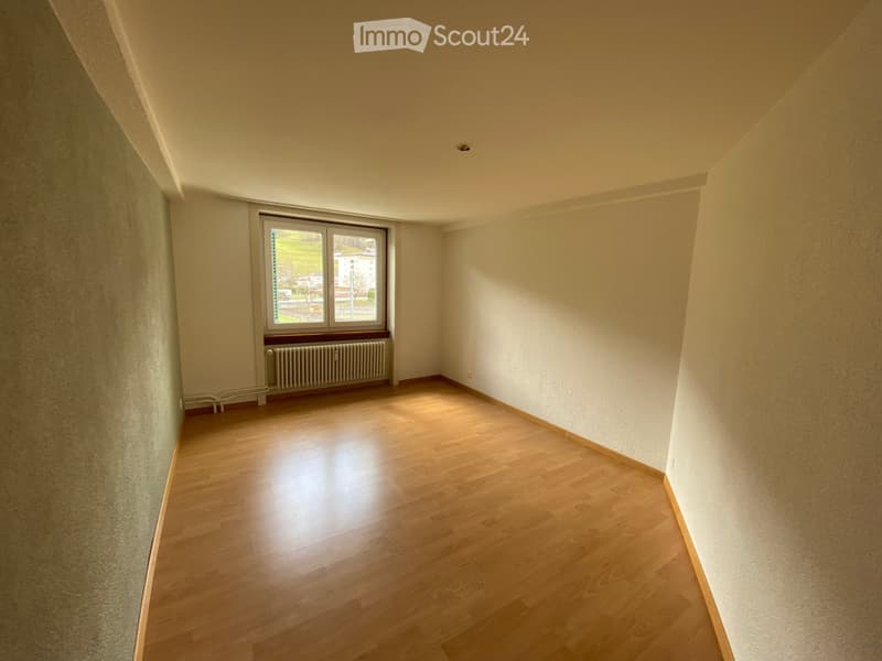 Empty room with wooden flooring, white walls, and a window with a radiator below it.