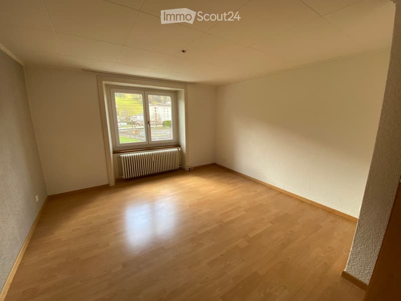 Empty room with wooden flooring, white walls, and a window with a radiator below it.