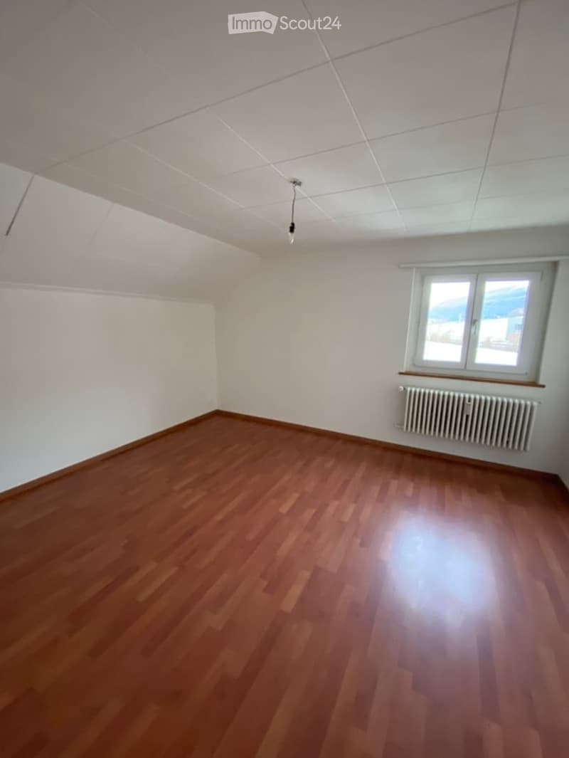 Completely empty room with wooden flooring, white walls, and a single window with a radiator below it.