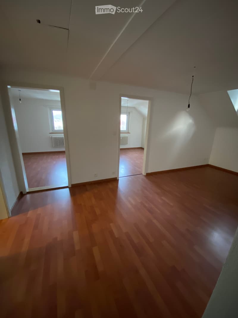Empty room with wooden flooring, white walls, and two open doorways leading to adjacent rooms with windows and radiators.