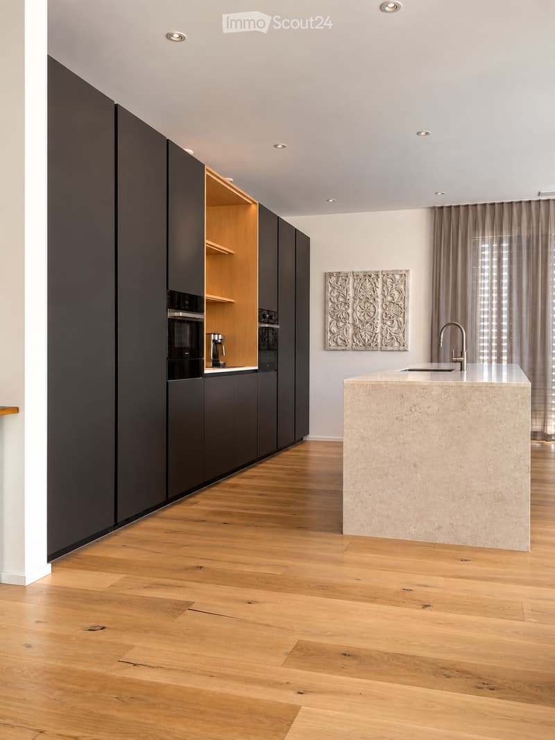 Modern kitchen with dark cabinets, light wooden floor, central island with marble countertop, and a sink with a modern faucet.