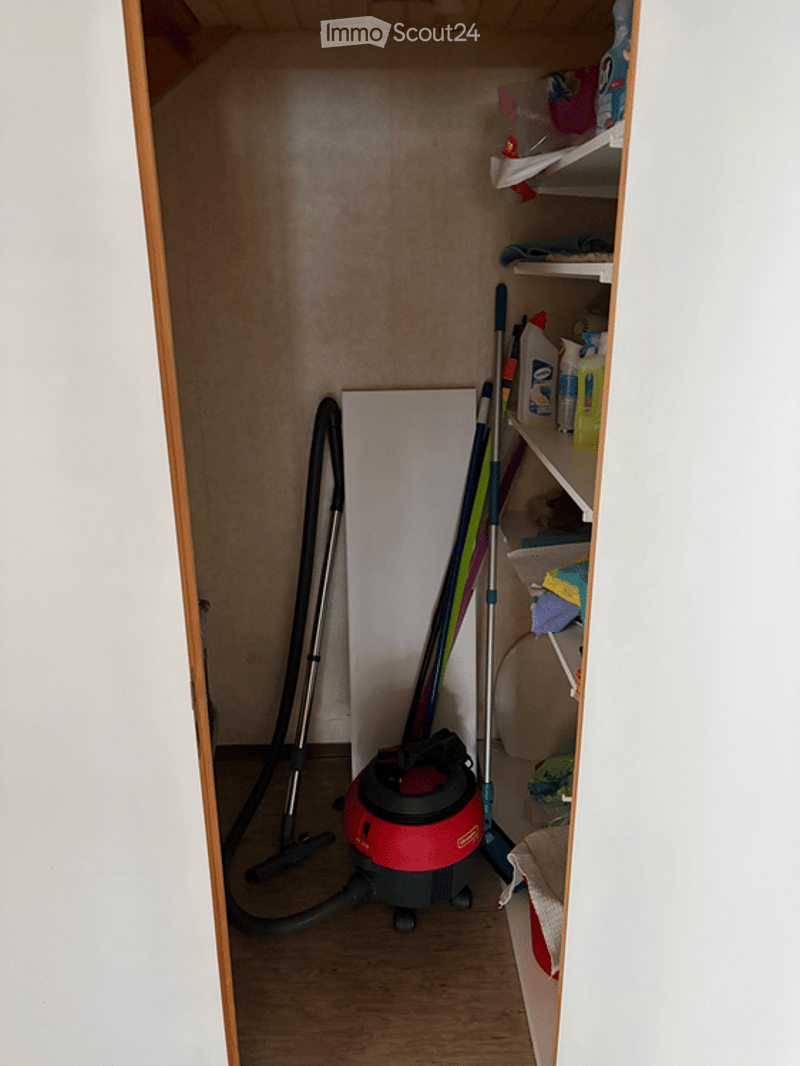 A small utility closet with a vacuum cleaner, broom, mop, and cleaning supplies on shelves.