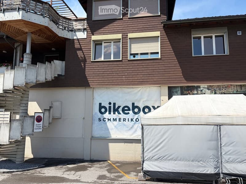 Two-story building with brown wooden facade, multiple windows, and a balcony on the upper level. A sign reading "bikebox SCHMERIKO" is displayed on the lower level.
