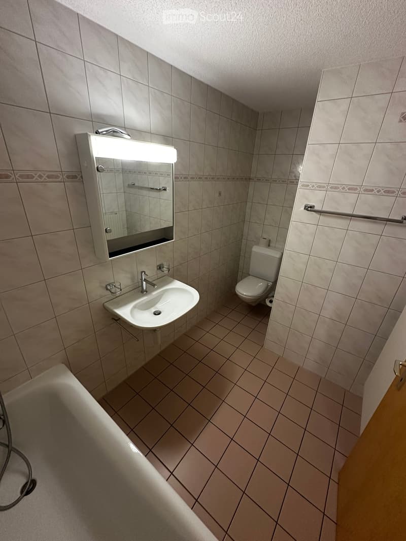 Clean bathroom with beige tiles, a white sink, a toilet, a bathtub, and a mirror with built-in lighting.