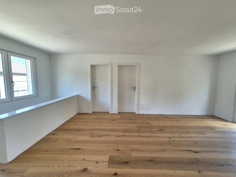 Empty room with wooden flooring, white walls, two doors, and a window with a view of a roof.