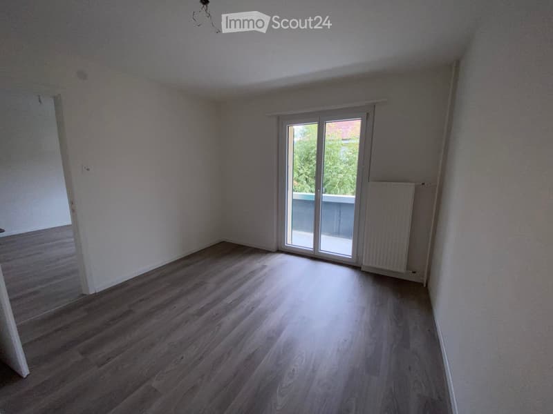 Empty room with wooden flooring, white walls, and a sliding glass door leading to a balcony.