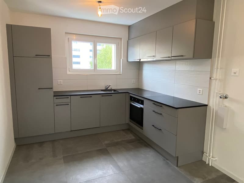 Modern kitchen with grey cabinets, a sink, and an oven, featuring tiled walls and a tiled floor.