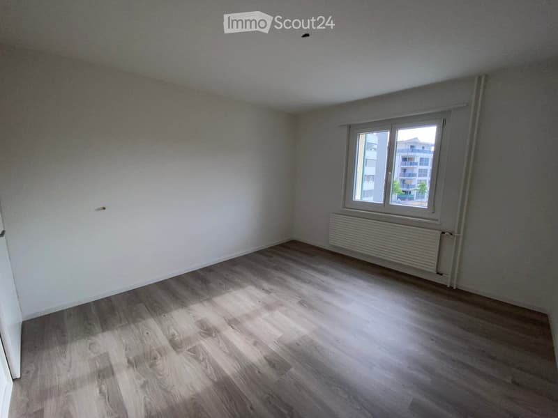 Empty room with wooden flooring, white walls, and a window with a radiator below it.