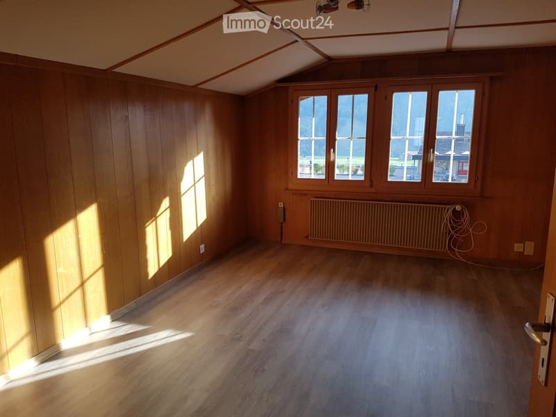 Empty room with wooden walls and flooring, large windows, radiator, and visible electrical outlets.
