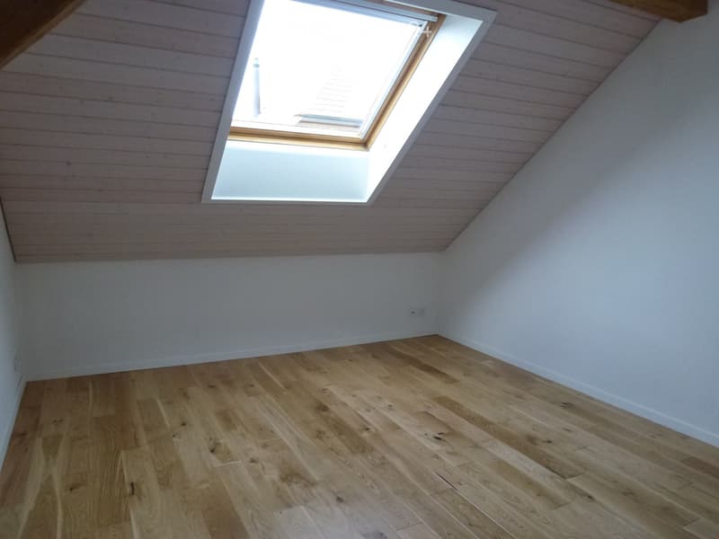 Empty room with wooden flooring and white walls, featuring a skylight window in the sloped ceiling.