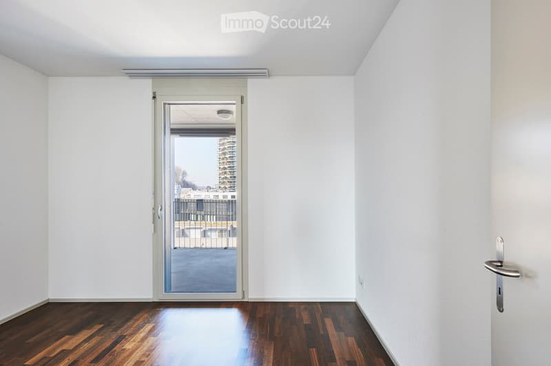 Empty room with white walls, wooden flooring, and a large sliding glass door leading to a balcony or outdoor area.
