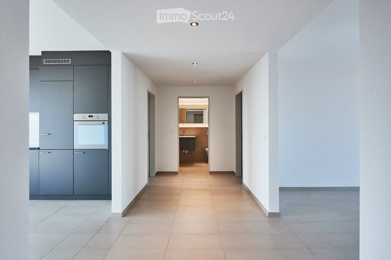 Modern hallway with tiled flooring, white walls, recessed lighting, and access to a kitchen and bathroom area.