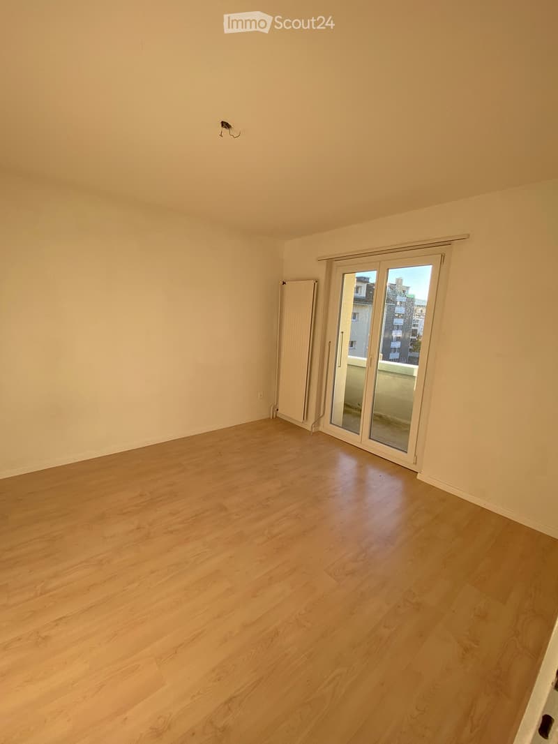 Empty room with light wooden flooring, white walls, and a large sliding glass door leading to a balcony.