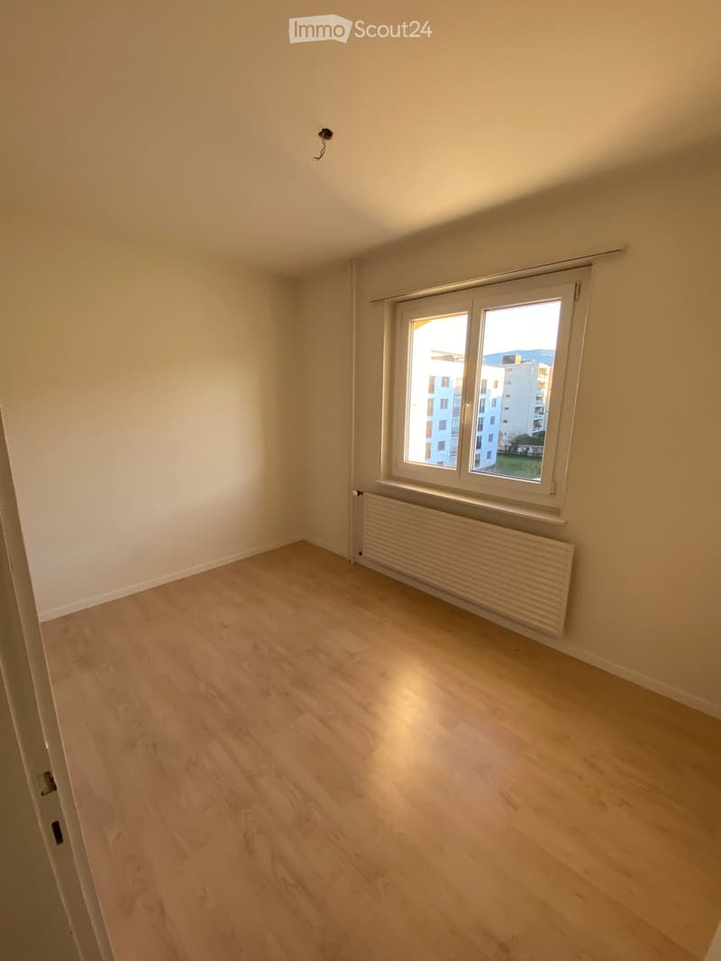 Empty room with light wooden flooring, white walls, and a large window with a radiator below it.