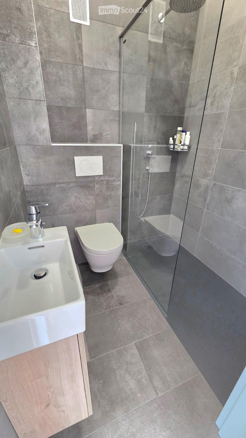 modern bathroom with white sink, white toilet, glass shower enclosure, gray tiles