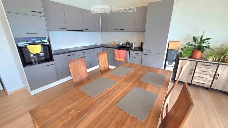 modern kitchen with wooden table, gray cabinets, black countertops, oven, washing machine, plants