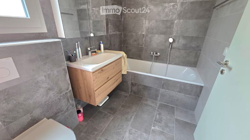 Bathroom with gray tiles, white bathtub, wooden cabinet, white sink, mirror, and shower head