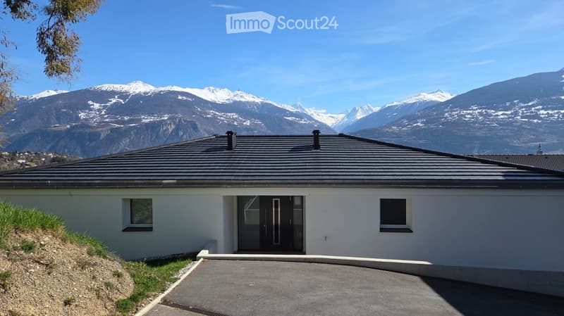 Modern white house, black roof, large windows, driveway, snowy mountains in the background