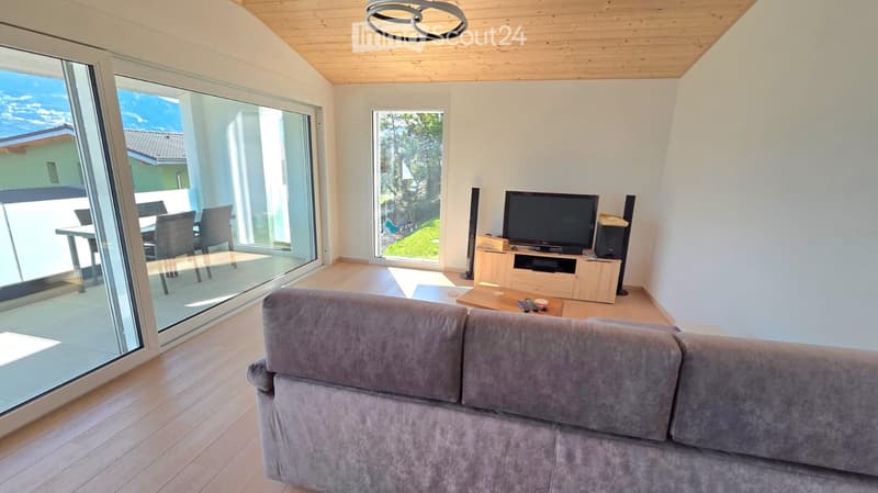 wooden floor, large windows, balcony, gray couch, TV, speakers, wooden table, remote controls
