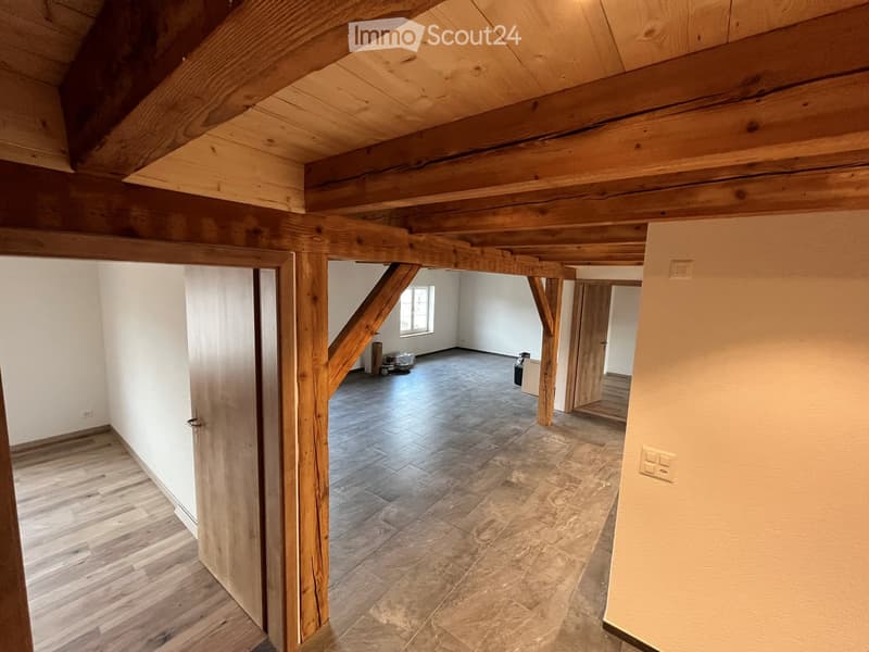 Empty room with exposed wooden beams, wooden flooring, and tiled flooring in an adjacent area. No furniture or equipment visible.