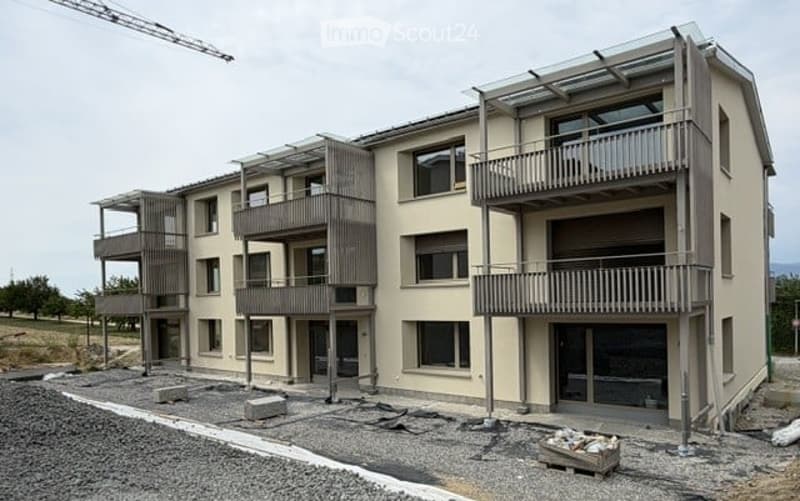 Modern multi-story residential building with balconies and large windows, under construction with visible scaffolding and materials.