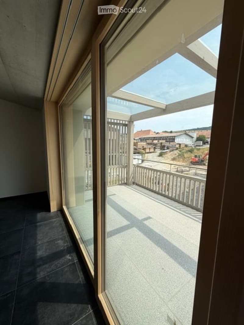 Balcony with a view of the surrounding area, featuring a wooden railing and a glass door leading to the interior.