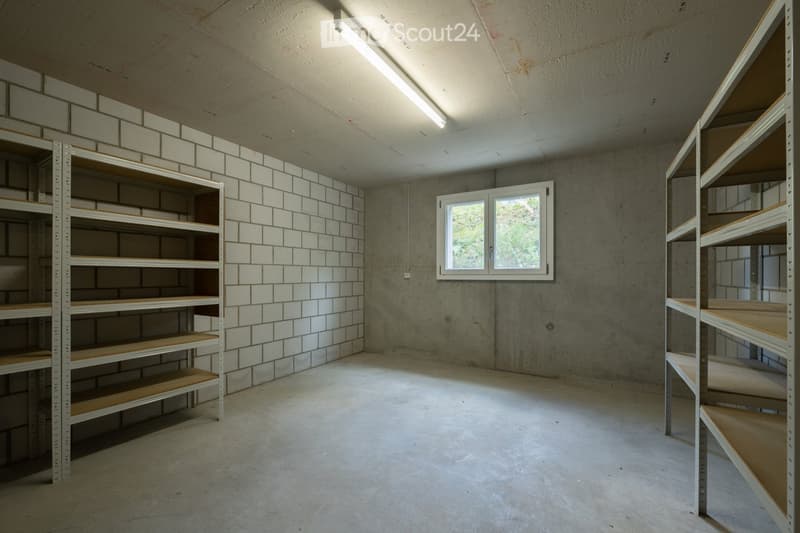 Empty room with concrete walls and floor, white tiled backsplash, metal shelving units, and a single window letting in natural light.