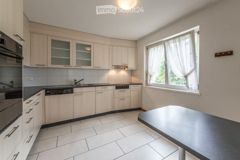 Modern kitchen with light wood cabinets, stainless steel appliances, a central island, and a large window with white curtains.